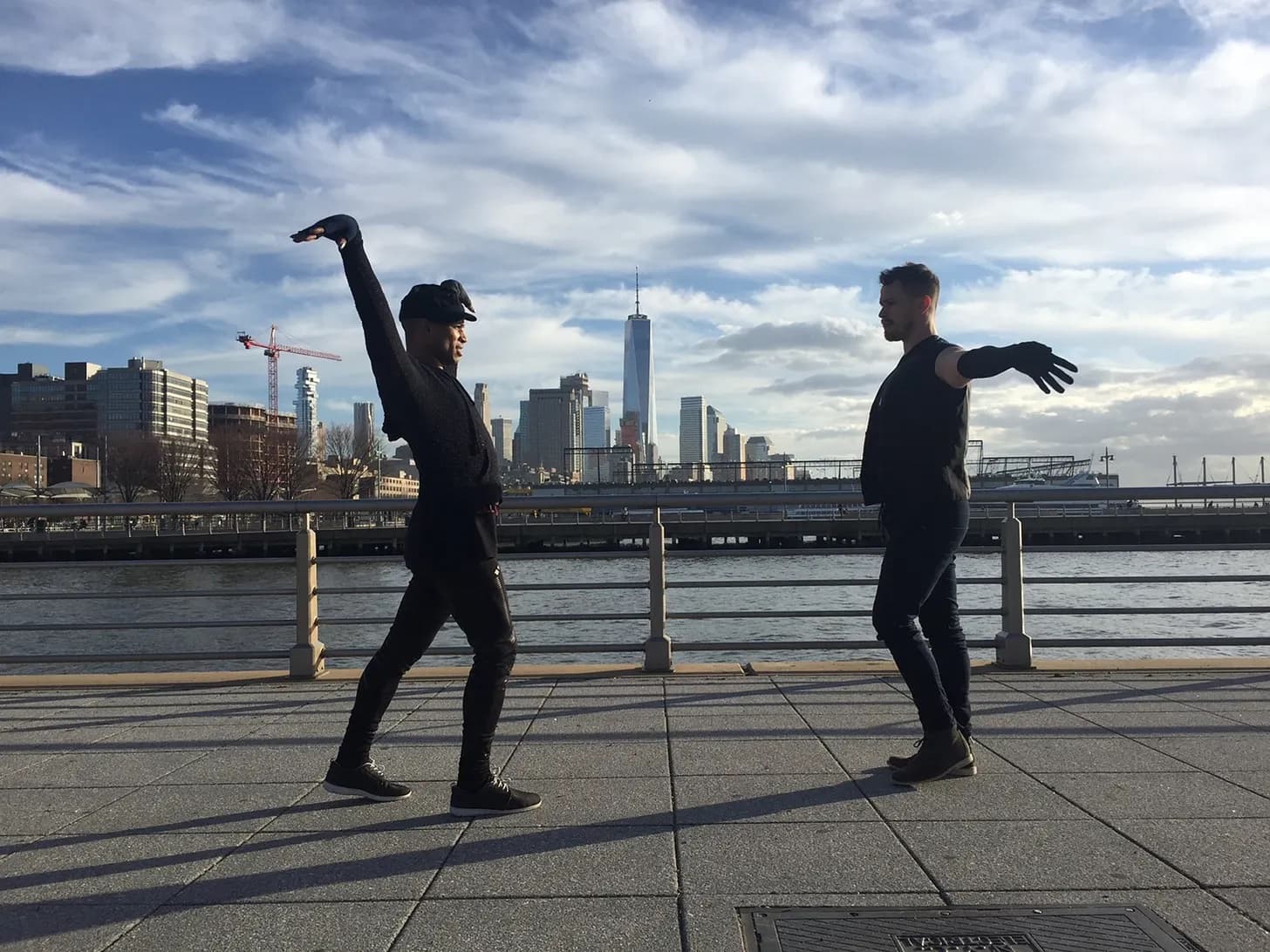 Two dancers facing each other on a Hudson River pier, the Manhattan skyline behind them