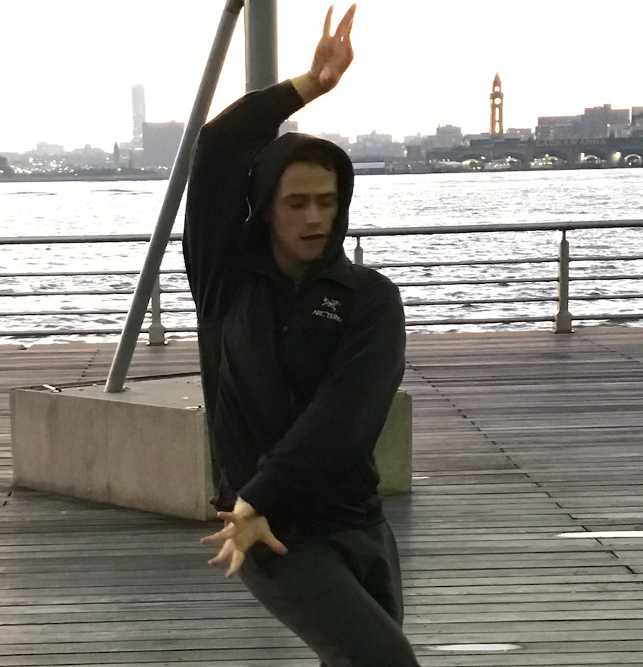 Russell Patrick Brown bailando en un muelle de madera, con el río Hudson y la torre del reloj de Hoboken detrás